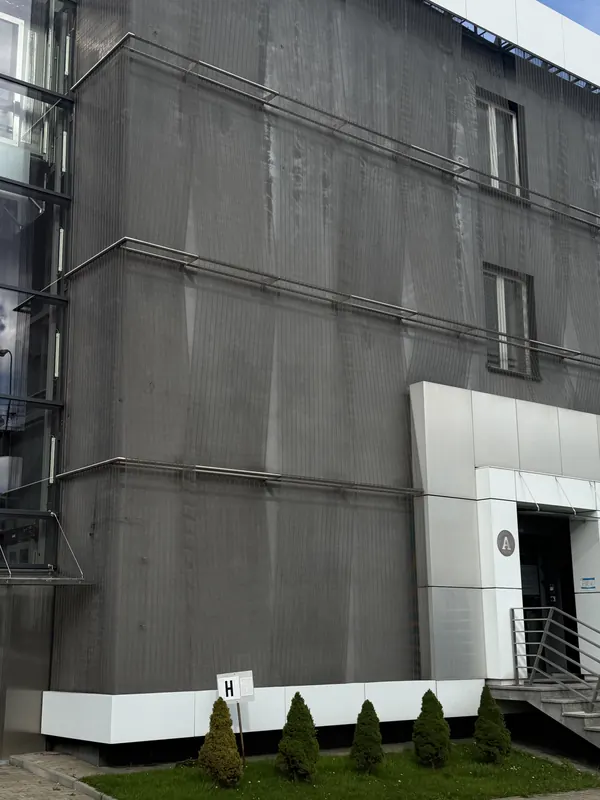 Πρόσοψη κτιρίου με κατακόρυφα φύλλα ανοξείδωτου μεταλλικού πλέγματος μπροστά από τα παράθυρα